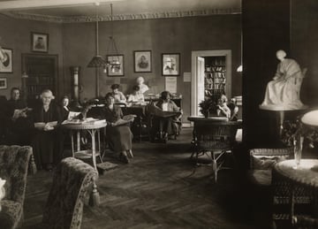 Et gammelt svart-hvitt bilde av et leserom der flere personer sitter og leser ved bord og i stoler.