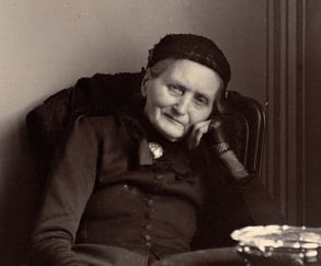 Eldre person sittende i en stol innendørs, med hodet hvilende på hånden. Historisk portrettfotografi i svart-hvitt.