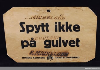 Plakat fra Norske Kvinners Sanitetsforening med teksten: «Spytt ikke på gulvet». Et historisk hygieneskilt som oppfordrer til å unngå spytting innendørs for å forebygge smitte.