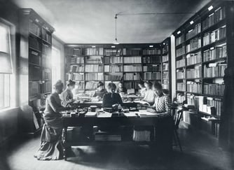 Kvinner sitter rundt bord i et bibliotek