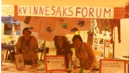 Tre kvinner kak et bord med brosjyrer og plakater og banner med "kvinnesaksforum"
