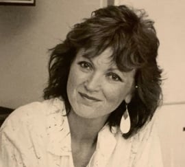 Et svart-hvitt portrettfoto av en kvinne med mørkt, mellomlangt hår og en stor øredobb, fotografert innendørs.