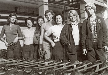 Et svart-hvitt gruppebilde av flere kvinner som står i et industrielt miljø, med metallgjenstander i forgrunnen.