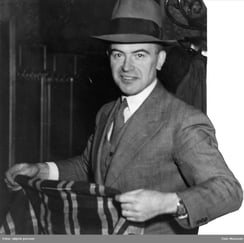 Svart-hvitt bilde av mann med dress og hatt.