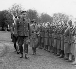 Historisk svart-hvitt-foto av uniformerte personer oppstilt på rekke under en militær inspeksjon på en gresslette.