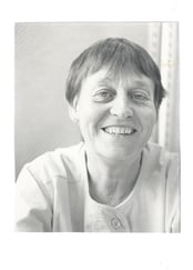 Svart-hvitt portrettfoto av en kvinne med kort hår, fotografert innendørs mot en lys bakgrunn.