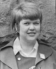 Historisk svart-hvitt portrettfoto av en kvinne med kort hår, fotografert foran en steinvegg.