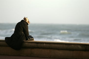 Kvinne sitter på en mur ved havet.