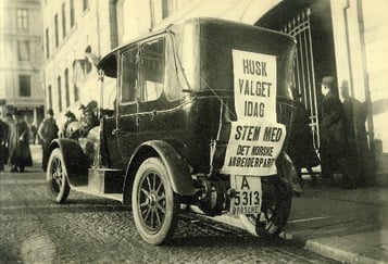 Bilde av gammeldags bil med plakat på baksiden.