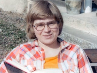 Fotografi av kvinne med rutete skjorte, briller, kort hår med bok.