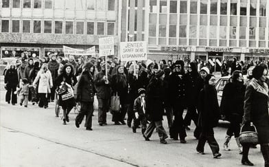 8. mars demonstrasjon, bygate i Trondheim. Paroler: "Kvinner, fagorganiser dere!", "Jenter, skaff dere utdanning!", "Barn… er ikke bare kvinnens ansvar".