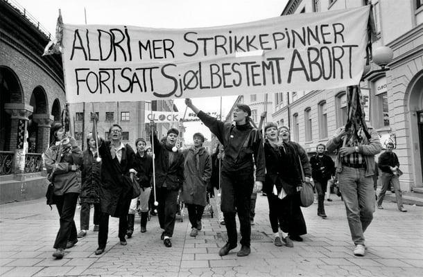 svart-hvitt bilde av en gruppe kvinner i demonstrasjonstog med et banner som lyder aldri mer strikkepinner fortsatt sjølbestemt abort.