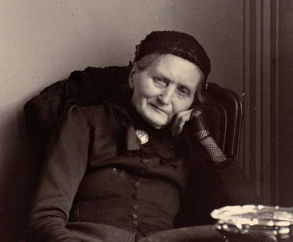 Eldre person sittende i en stol innendørs, med hodet hvilende på hånden. Historisk portrettfotografi i svart-hvitt.