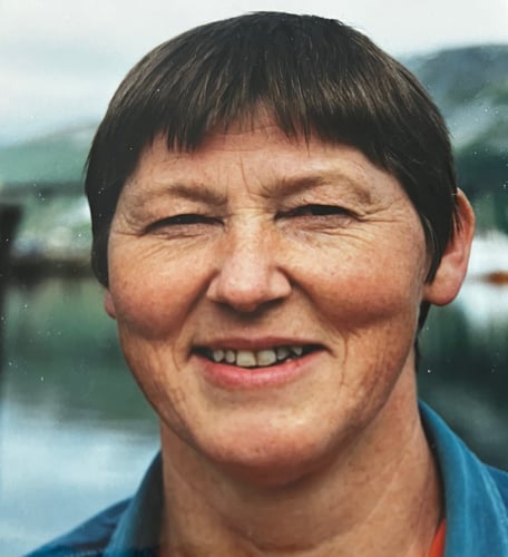 Portrettfoto av en kvinne med kort hår, fotografert utendørs med vann og landskap i uskarp bakgrunn.