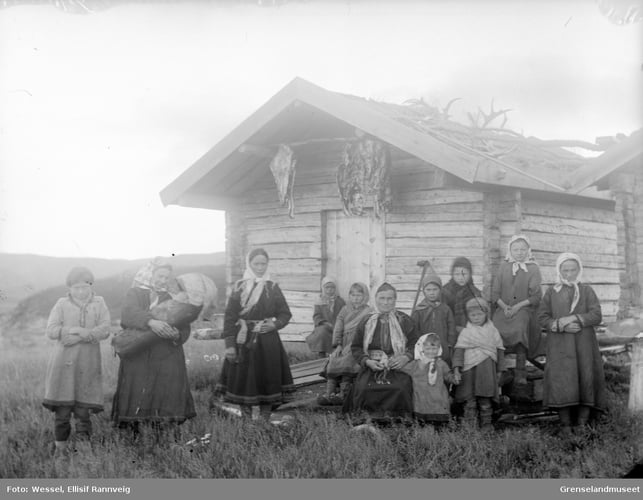 En gruppe samiske kvinner og barn fotografert utenfor et tømmerhus, trolig i Pasvik 