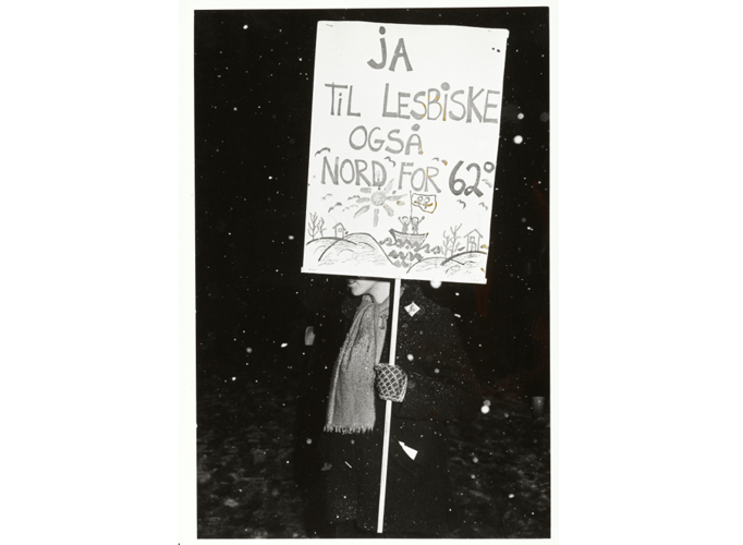 Kvinne i snødriv holdende og delvis skjult bak plakat: Ja til lesbiske også nord for 62 grader.