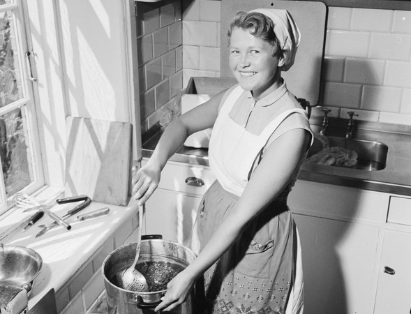 Svart-hvitt bilde av en blid husmor som rører i en gryte.