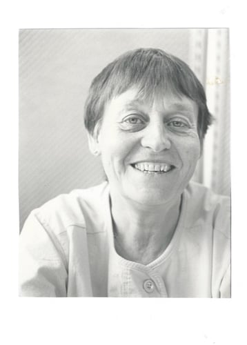 Svart-hvitt portrettfoto av en kvinne med kort hår, fotografert innendørs mot en lys bakgrunn.