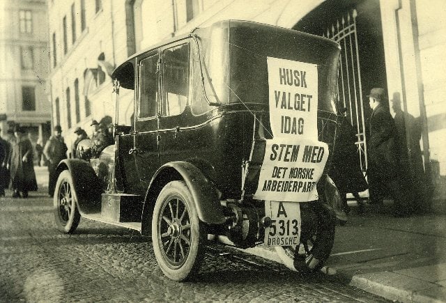 Bilde av gammeldags bil med plakat på baksiden.
