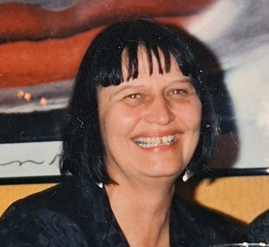 Et fargeportrett av en kvinne med kort, mørkt hår, fotografert innendørs foran et kunstverk eller bilde i bakgrunnen.