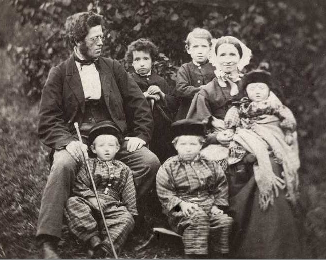 Svar-hvitt familiebilde med mor, far og fem barn i gammeldagse klær.
