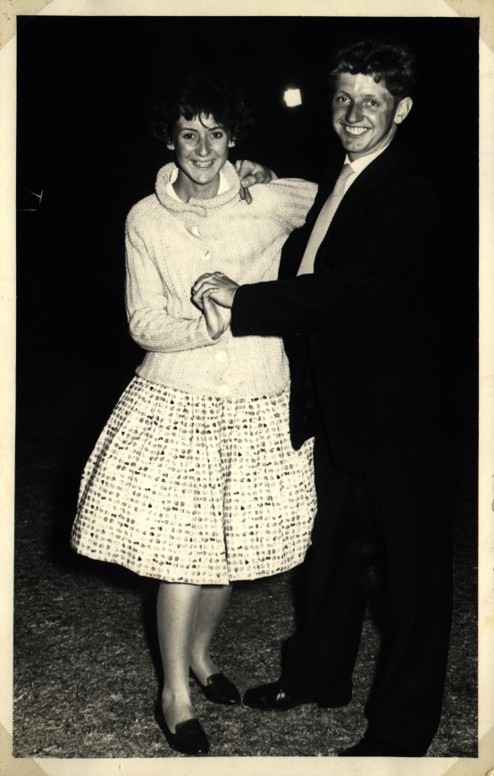 Bilde av et ungt smilende par som danser. Kvinnen i hvit kjole og mannen i svart dress. 
