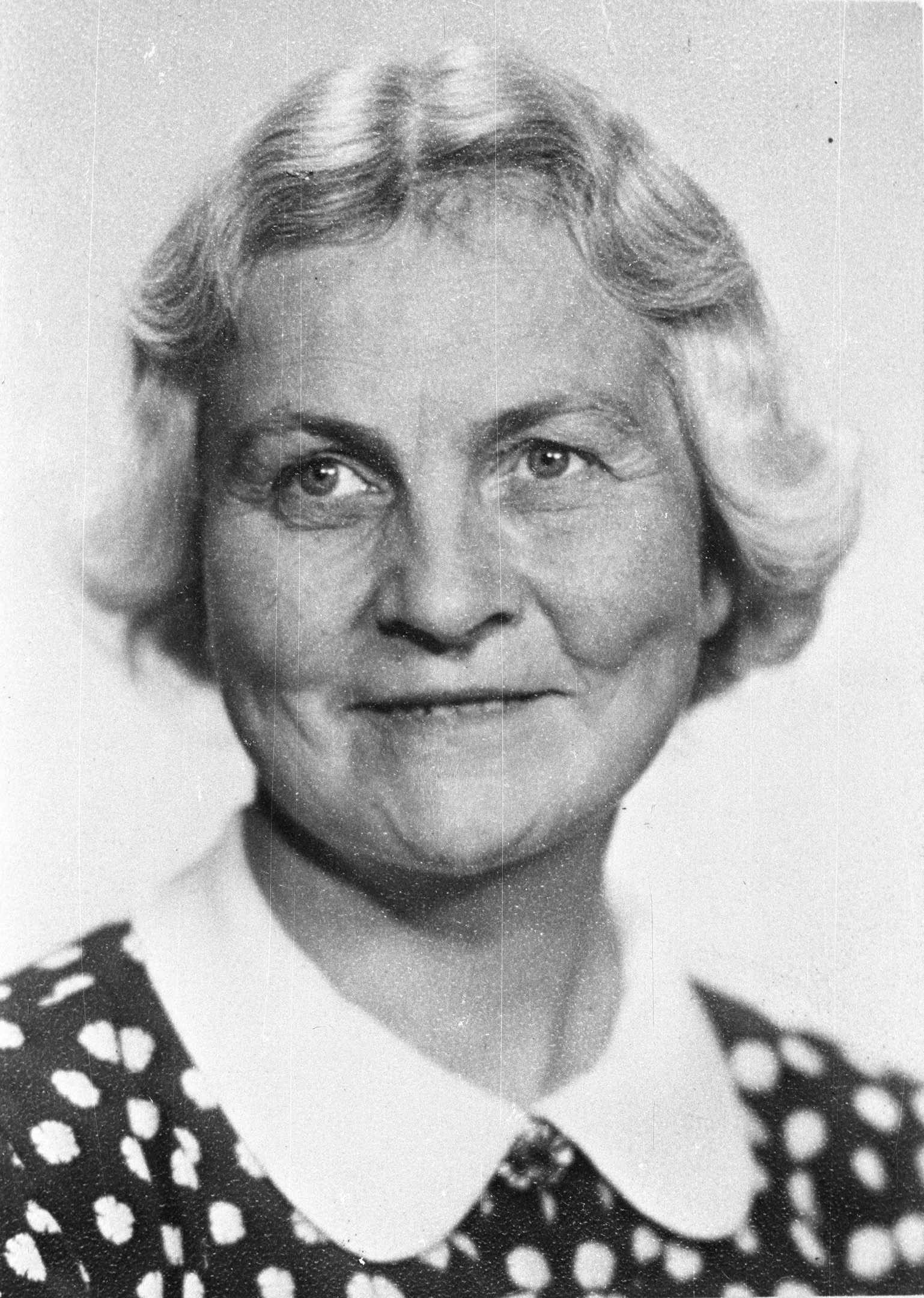 Portrett av kortklippet kvinne med blondt hår og kjole med krage. 
