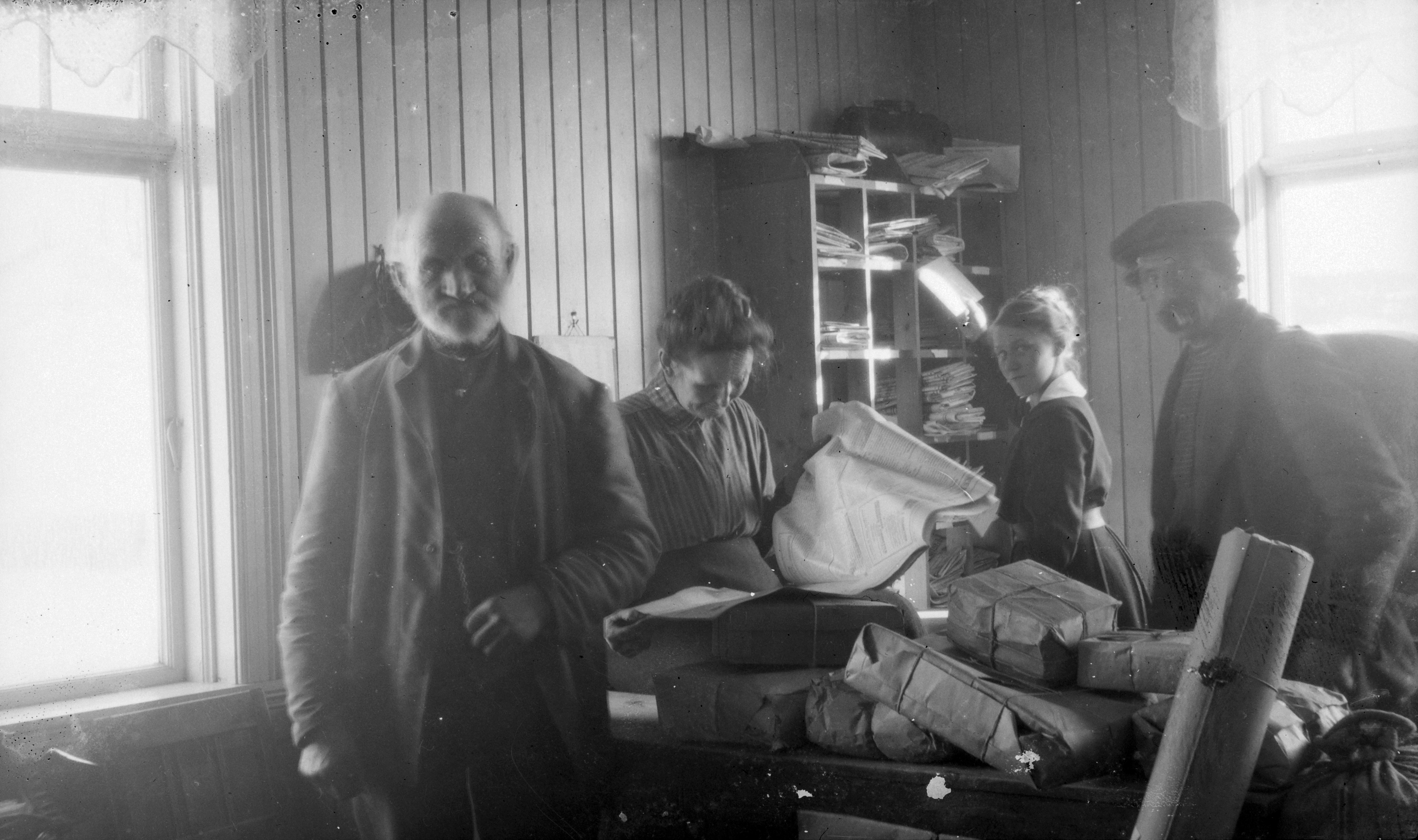 Interiør posthus, 4 postarbeidere, kvinner og menn, hyller, brev, paller.