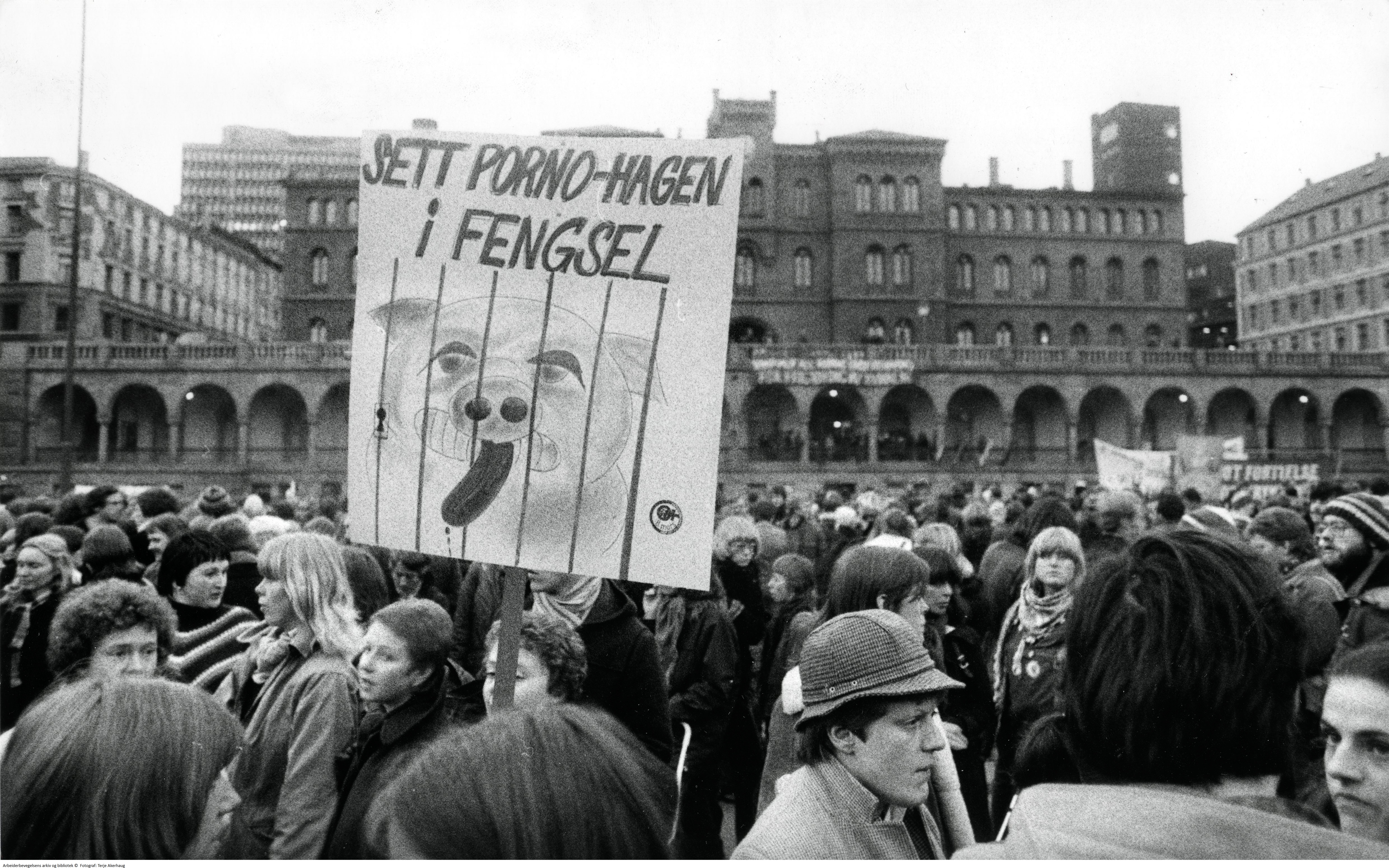 Demonstrasjon, folkemengde på Youngstorget i Oslo. Plakat med "Sett porno-Hagen i fengsel" illustrert med tegning av gris i bur. 