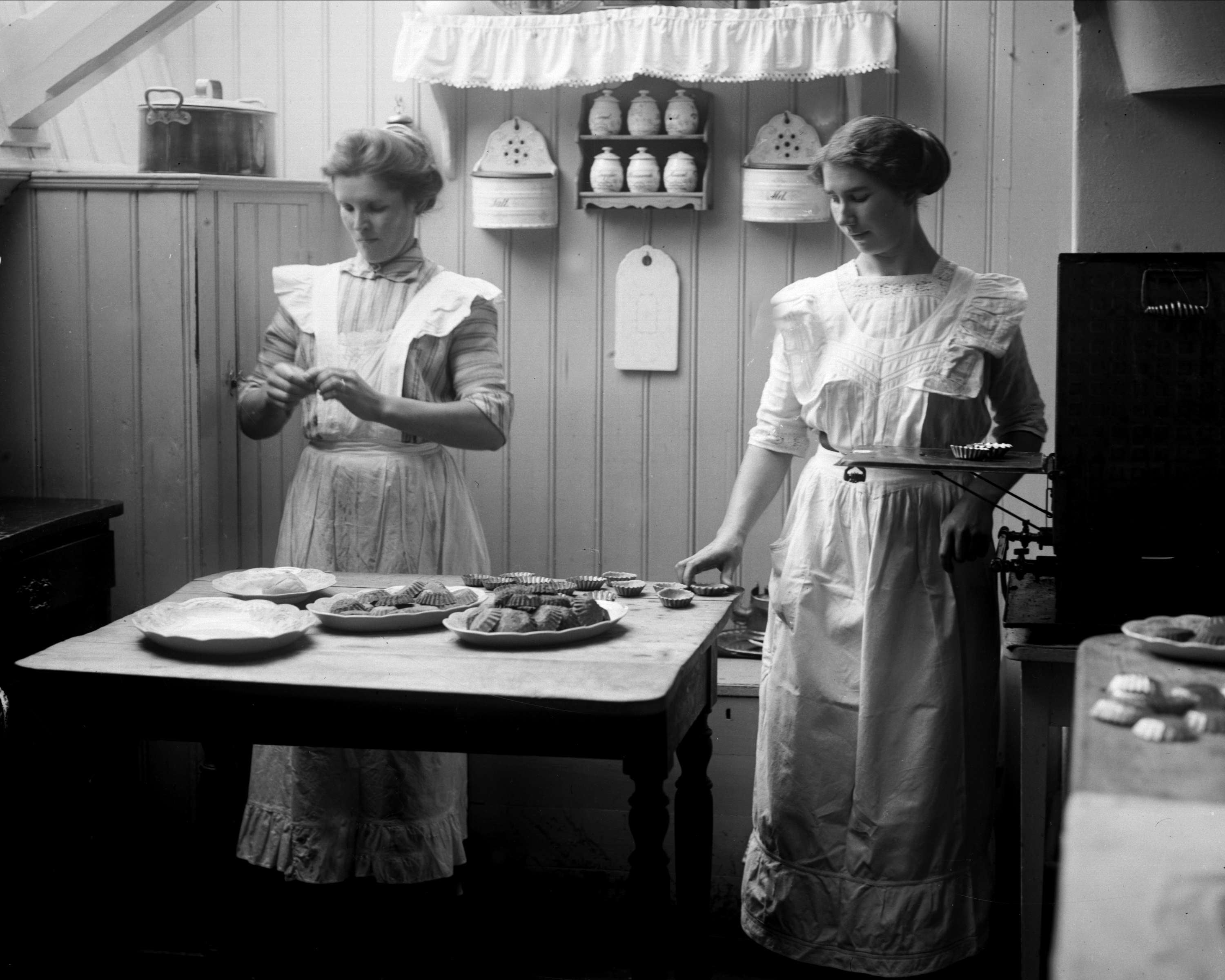 Interiør, kjøkken med to tjenestepiker som baker sandkaker.