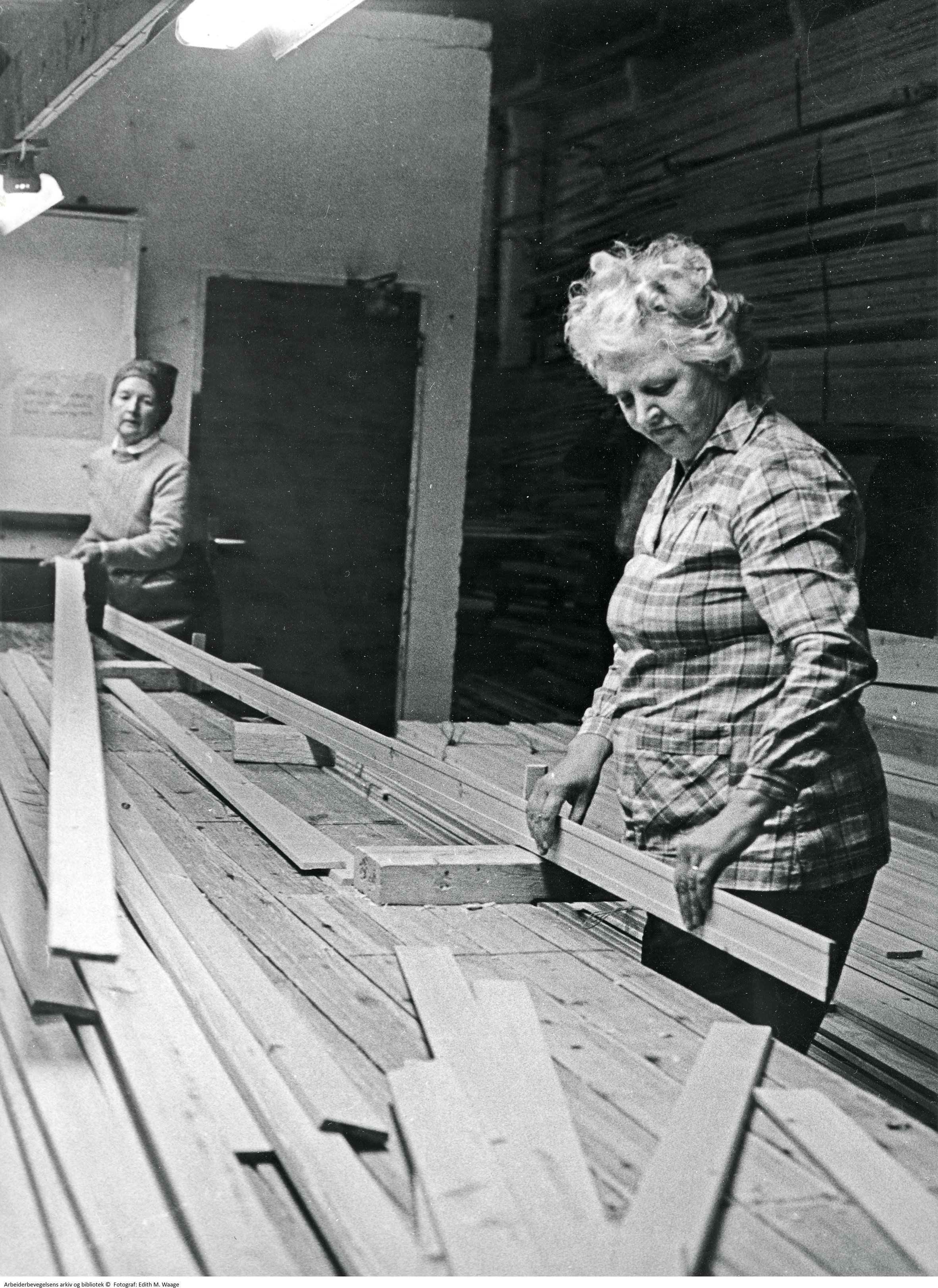To kvinner sorterer plank i fabrikklokale.