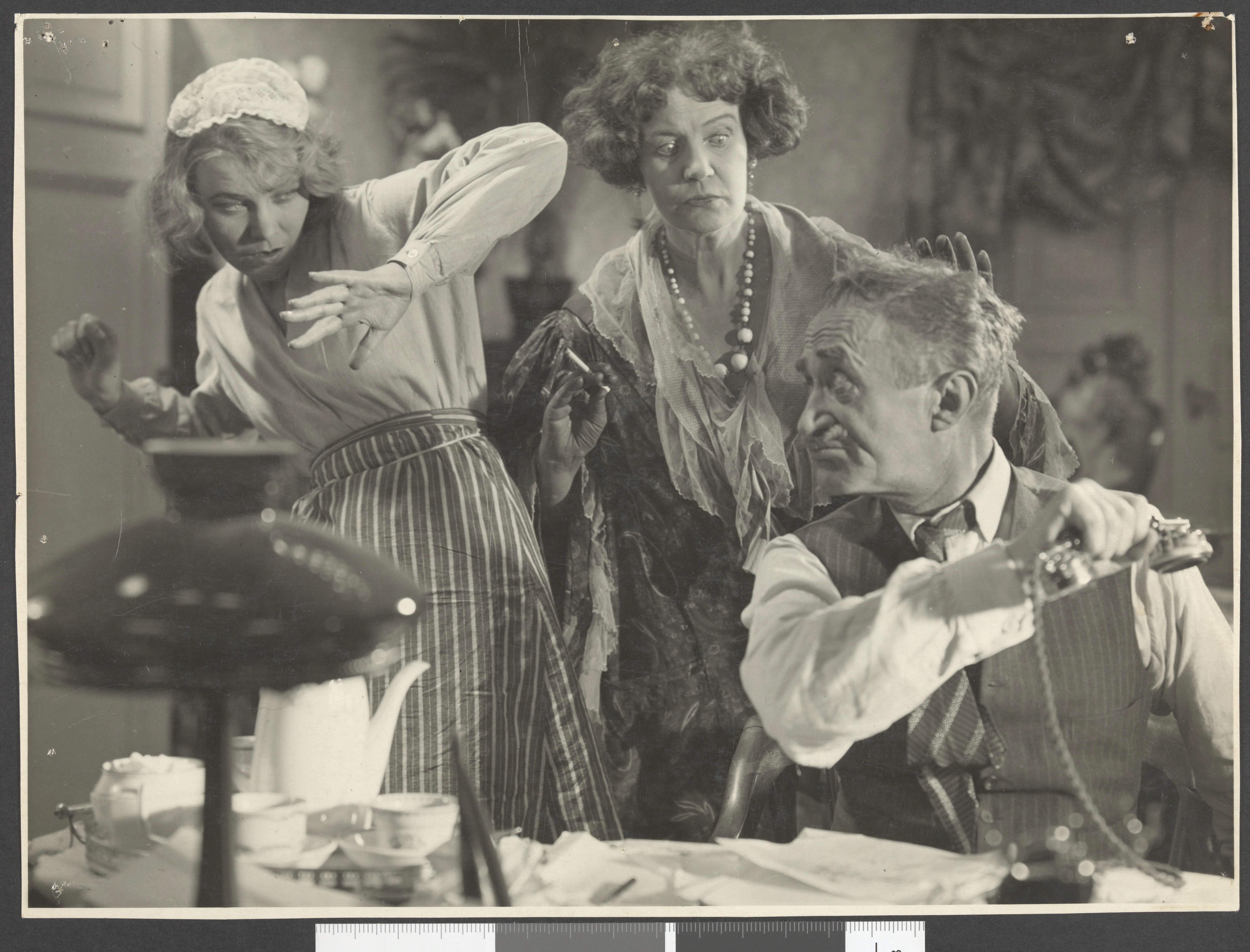 Svart-hvitt bilde av to kvinner og en mann i scene fra filmen Vi som går kjøkkenveien.