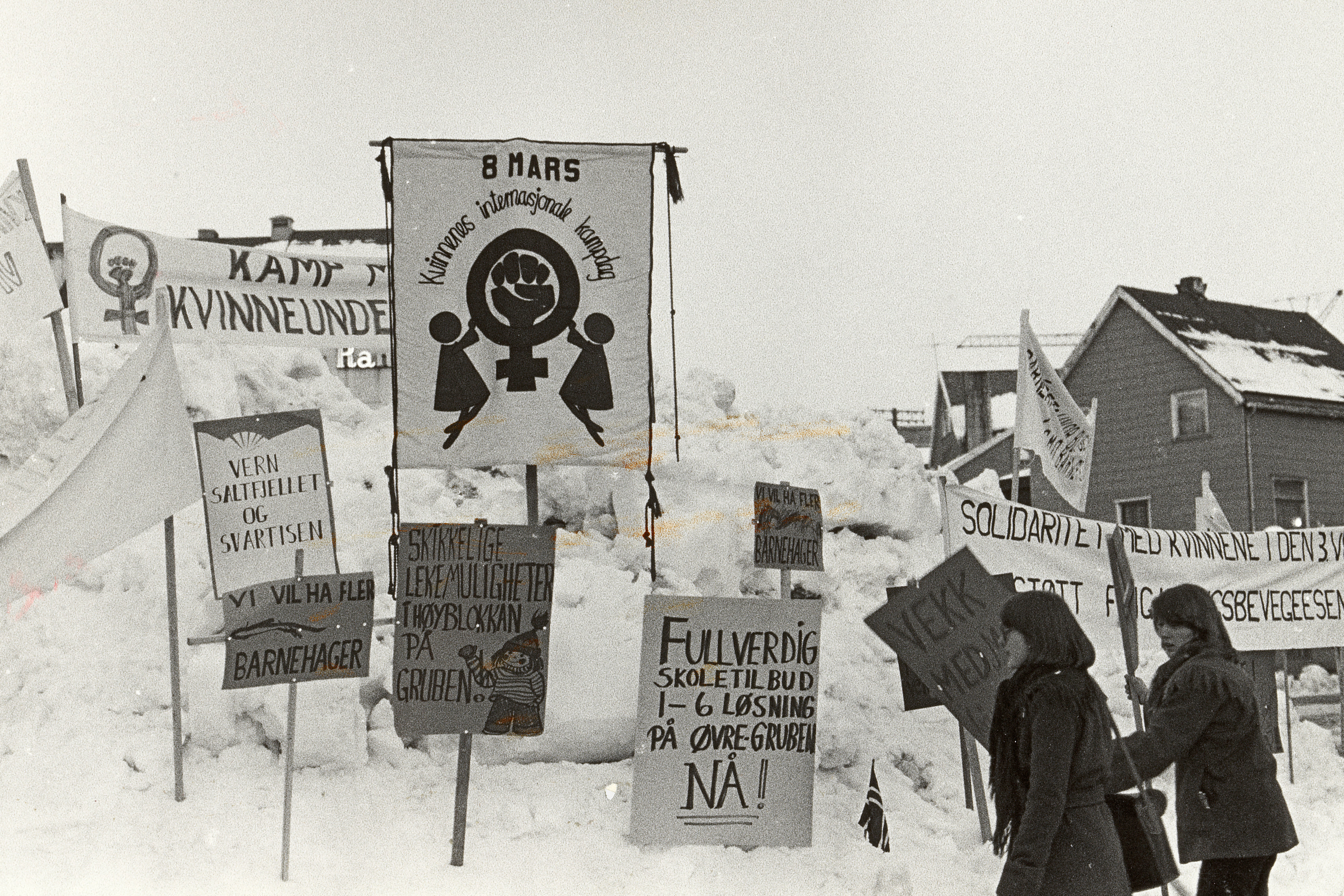 Plakater i snøfonn. Kvinner setter plakater i snøen.