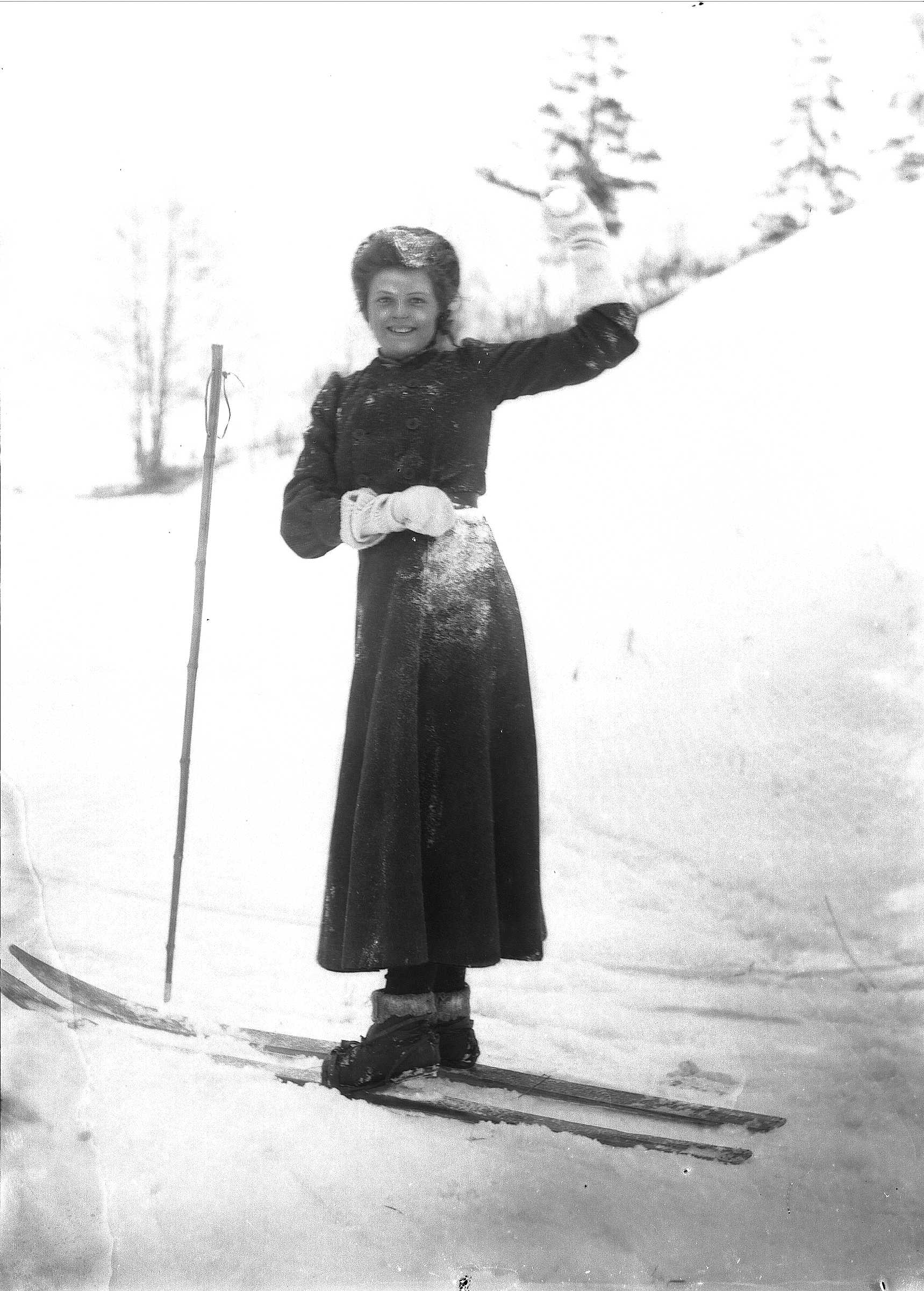 Kvinne i snødekt landskap. Kaster en snøball ble ski på beina.