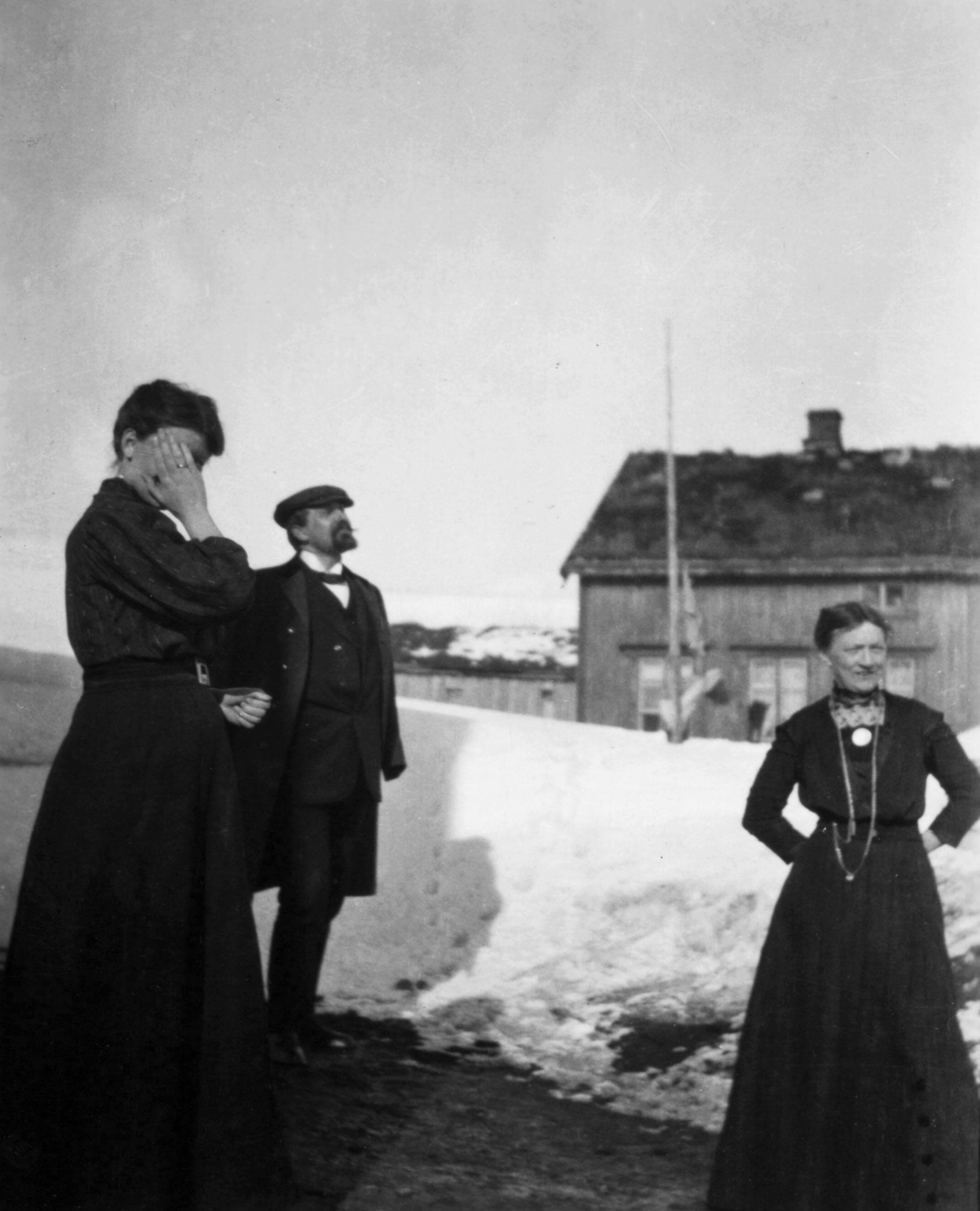 Gruppebilde to kvinner og en mann foran snøskavl, trehus og fjord i Båtsfjord.